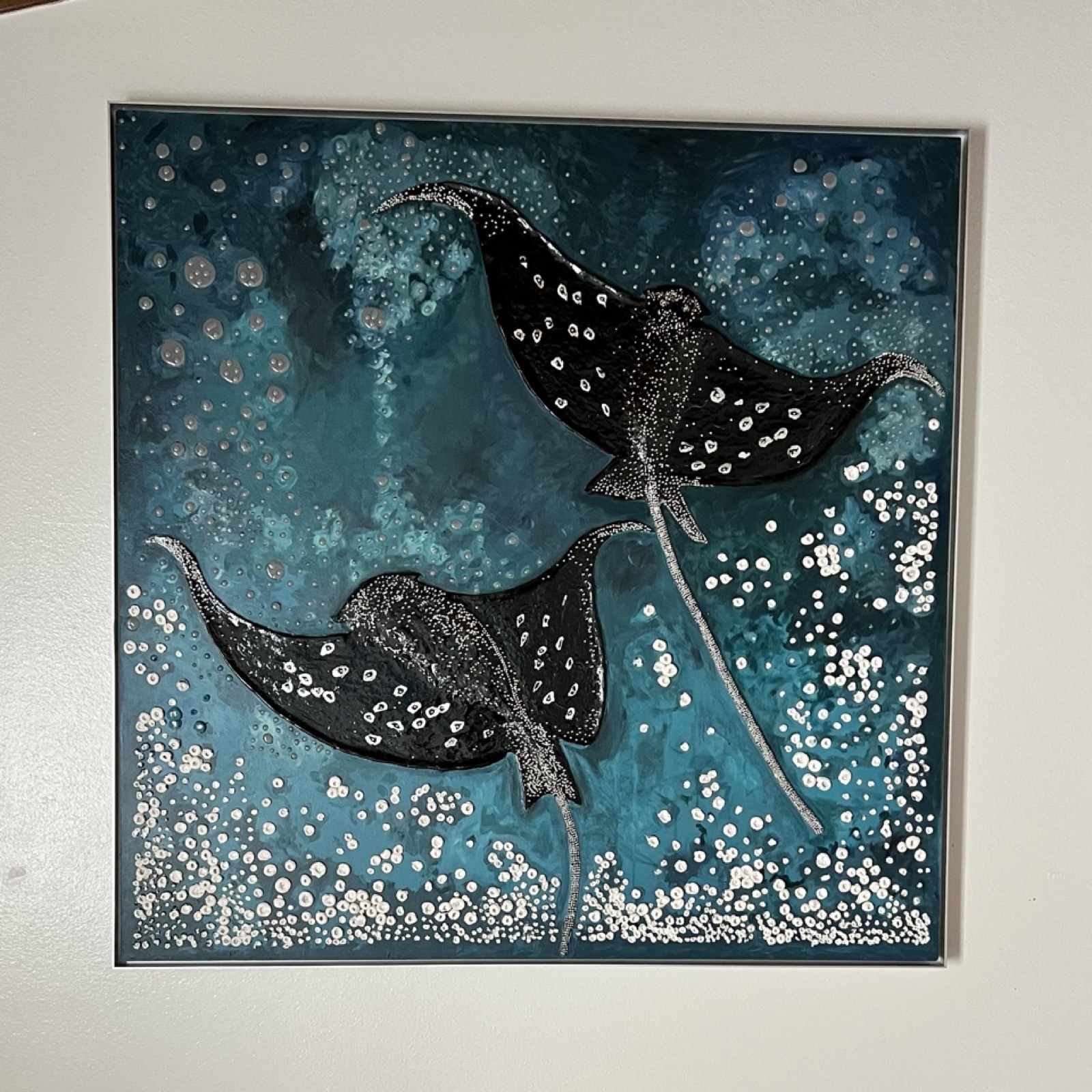 Two manta rays gliding through a teal sea scattered with white pearl dots